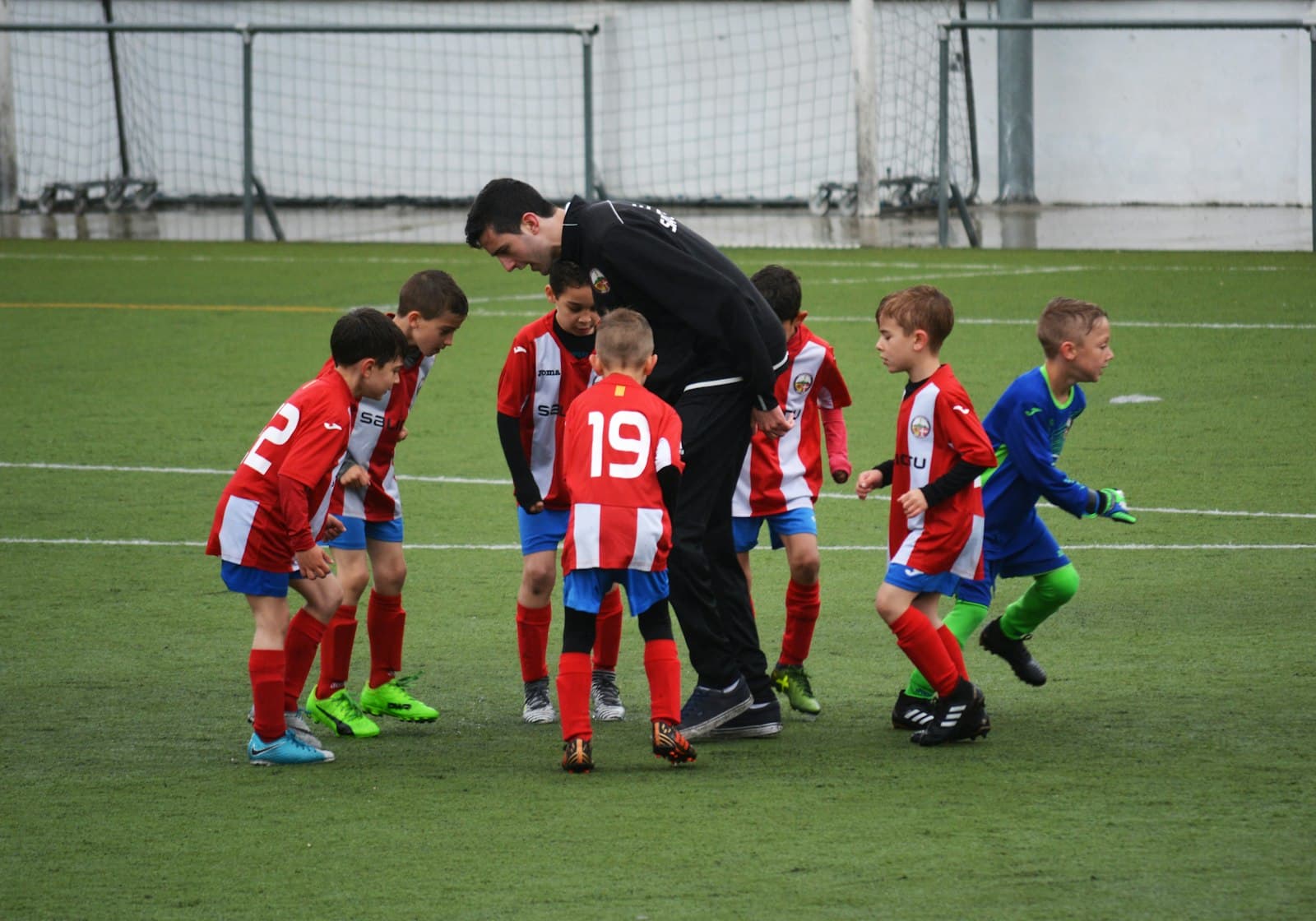 A youth football team huddled around their coach on an artificial pitch
